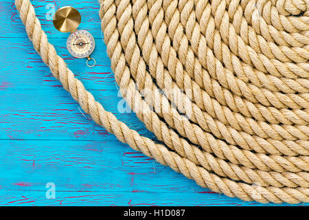 Neatly wound and coiled natural fiber rope with an open magnetic compass on a blue crackle paint wood background conceptual of n Stock Photo