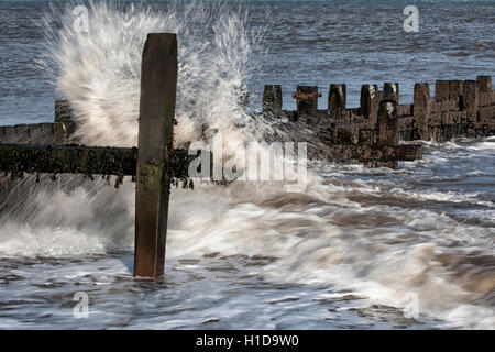 Sea water breaking through groynes on beach in slow motion Stock Photo