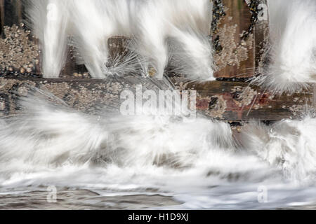 Sea water breaking through groynes on beach in slow motion Stock Photo