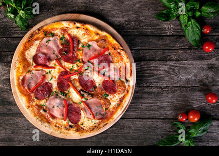 Delicious fresh Pepperoni pizza with salami , bacon , red pepper, green onions and cheese on the wooden background. Top view. Stock Photo