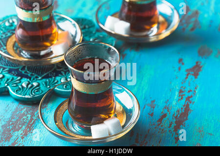 Turkish tea served in tulip shaped glass with two tiny sugar cubes on saucer on blue rustic table Stock Photo