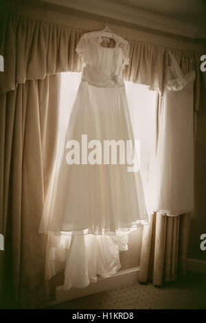 Brides wedding dress hanging up on the morning of the big day. Stock Photo