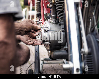 Mechanic with dirty hands fixing a screw on a old bike engine, intentional blur and vivid colors. Stock Photo