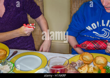 A family meal table set out with ahuge array of food for a celebratory christmas dinner , with family members pulling ctrackers adn touching drinking glasses. Stock Photo