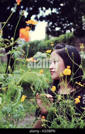 asian young girl hiding among flowers in garden Stock Photo