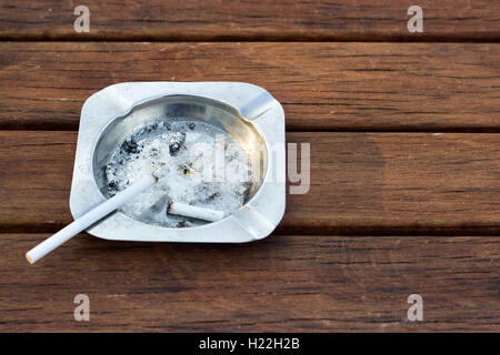 Metal ashtray with cigarette on wooden table Stock Photo