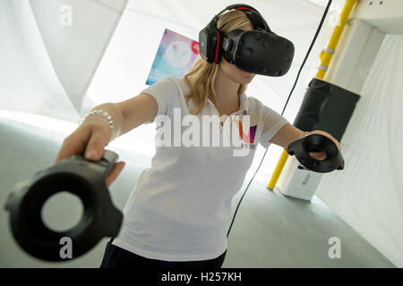 Nuremberg, Germany. 13th Sep, 2016. Janina Werner, co-founder of the Nuremberg start-up business 'Virtues', acts in a virtual world while wearing virtual reality glasses, two controllers for the hands and headphones in Nuremberg, Germany, 13 September 2016. The screen on the left shows the picture from his VR glasses. Virtual realities fascinate many people, but not all can afford the expensive equipment. The company 'Virtuis' wants take advantage of this. PHOTO: DANIEL KARMANN/dpa/Alamy Live News Stock Photo