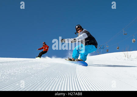 Snowboarders ride on blue sky backdrop in mountains Stock Photo