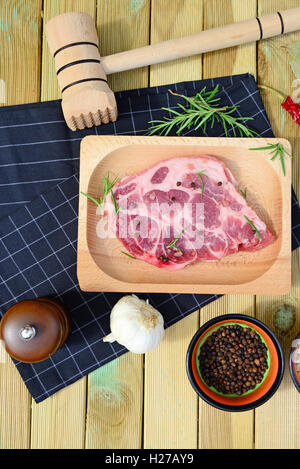 Raw pork meat on wooden plate, pepper mill, rosemary, spices and hammer on wooden background Stock Photo