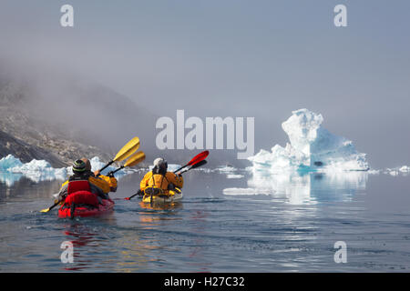 Sea kayakers paddling among icebergs on Sermilik Fjord near settlement of Tiniteqilaq, East Greenland Stock Photo