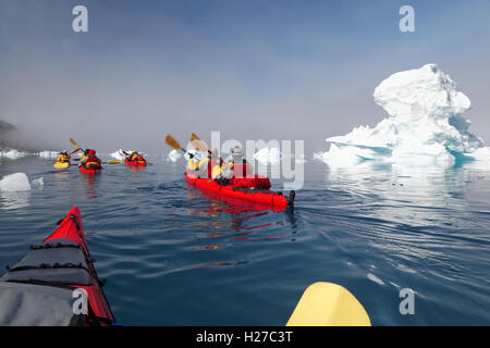 Sea kayakers paddling among icebergs on Sermilik Fjord near settlement of Tiniteqilaq, East Greenland Stock Photo