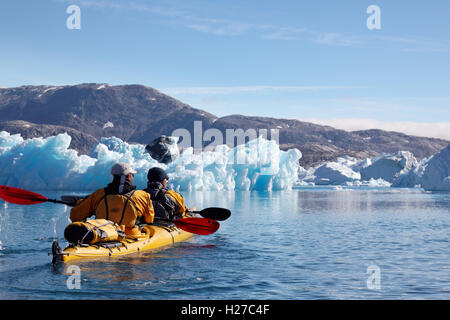 Sea kayakers paddling among icebergs on Sermilik Fjord near settlement of Tiniteqilaq, East Greenland Stock Photo