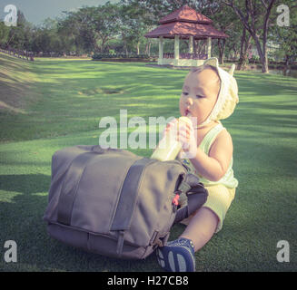 Adorable Asian baby boy drinking milk from bottle when picnic with family in the out door park, Soft pastel color effect Stock Photo