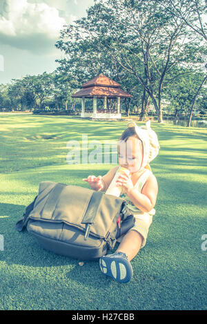 Adorable Asian baby boy drinking milk from bottle when picnic with family in the out door park, Soft pastel color effect Stock Photo