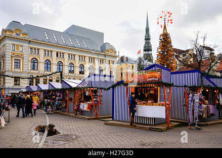 Riga, Latvia - December 26, 2015: People at the Christmas market with St Peter Church spire located on the Livu square in the center of the old town in Riga, Latvia. Stock Photo