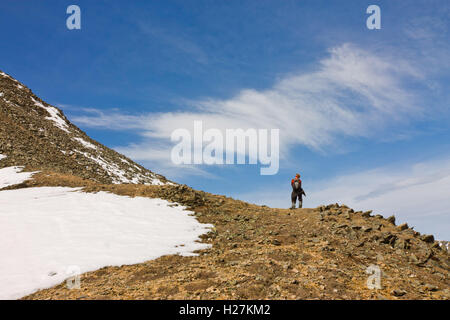 Tourist man with a backpack standing alone in the snow-capped mountains against the sky with cloud Stock Photo