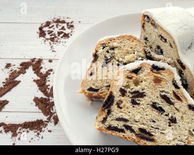 Stollen cake on the white plate and cocoa powder Christmas tree and showflake drawings Stock Photo