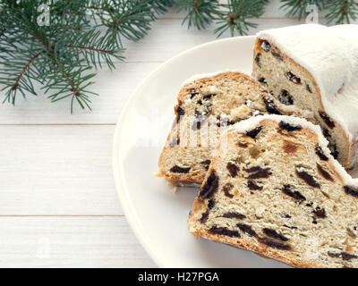 Stollen German Christmas cake on the white plate and blue spruce branches on the white wooden planks Stock Photo