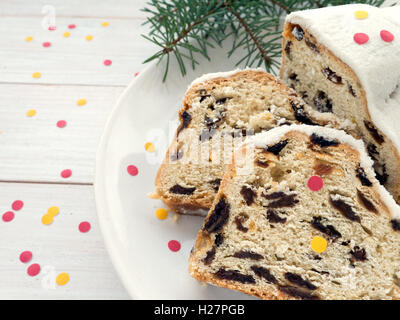 Stollen German Christmas cake on the white plate and blue spruce branches on the white wooden planks sprinkled with confetti Stock Photo