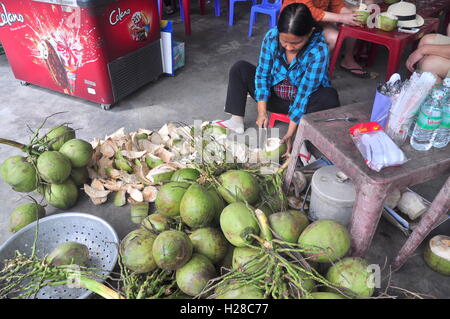 Nha Trang, Vietnam - February 7, 2016: A Vietnamese woman is cutting coconut for travellers on a treet vendor Stock Photo