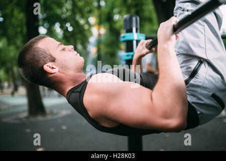 Young man doing pull ups on horizontal bar outdoors, workout, sp Stock Photo