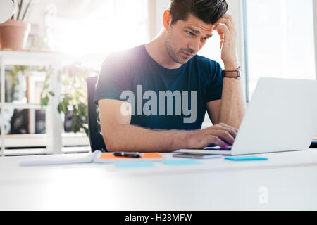 Shot of young man using laptop and looking worried. Businessman working at his desk. Stock Photo