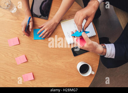 Top view of two business people sitting around a table and writing on post it notes. Brainstorming session with adhesive notes o Stock Photo