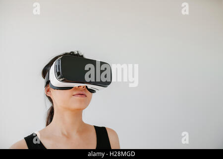 Shot of young woman using the virtual reality headset against grey background. Asian female model wearing VR goggles. Stock Photo