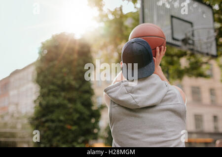 Rear view shot of a streetball player shoots basketball. Young guy playing basketball on outdoor court on a summer day. Stock Photo