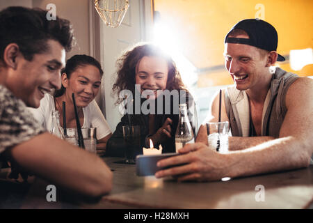 Cheerful young friends looking at smart phone while sitting in cafe. Mixed race people sitting at a table in restaurant using mo Stock Photo