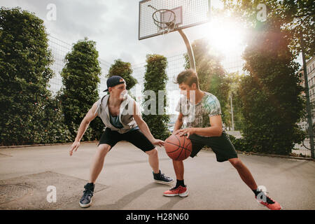 Teenage friends playing streetball against each other and having fun. Two young men having a game of basketball on outdoor court Stock Photo