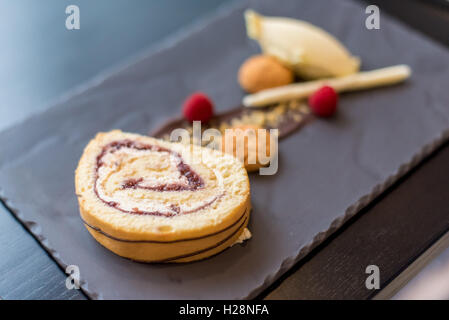 A Swiss roll sponge dessert with ice cream on a slate backdrop Stock Photo