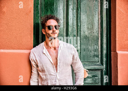 Handsome man leaning against old wall and green door in a summer day Stock Photo