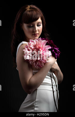 Auburn brunette english rose female portrait, black backdrop, purple lighting, wearing white jumpsuit with huge flowers Stock Photo