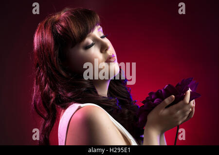 Auburn brunette english rose female portrait, red backdrop, purple lighting, wearing white jumpsuit with purple flower Stock Photo