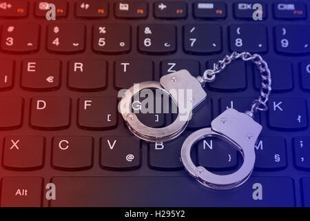 Cybercrime concept with small handcuffs on computer keyboard Stock Photo