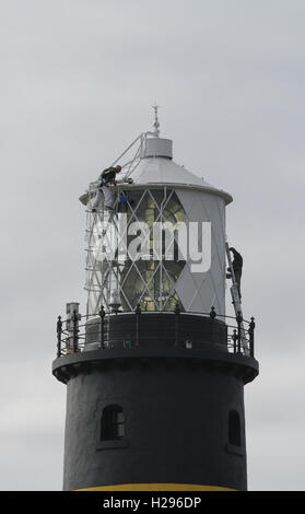 Two men on the roof of a lighthouse painting the lighthouse lamp tower on a grey day at St John's Point County Down Northern Ireland. Stock Photo