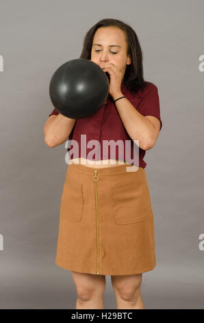 Adult female blowing up a huge black balloon. Stock Photo