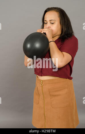 adult female blowing up a very large black balloon Stock Photo