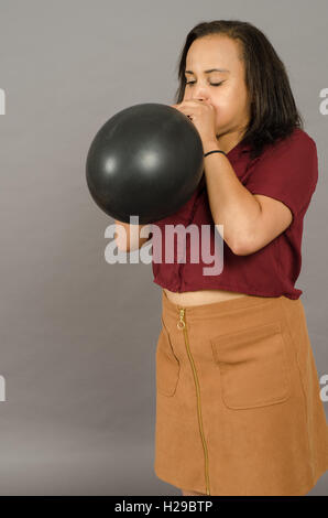 adult female blowing up a very large black balloon Stock Photo