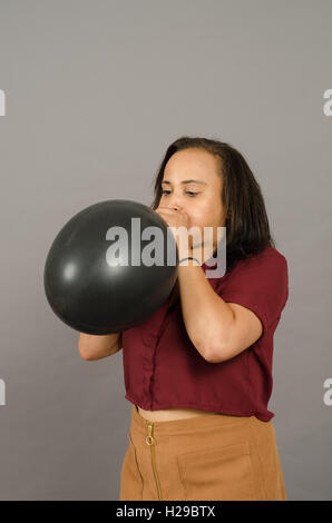 adult female blowing up a very large black balloon Stock Photo