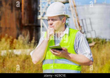 Thoughtful engineer using tablet PC near tanks Stock Photo