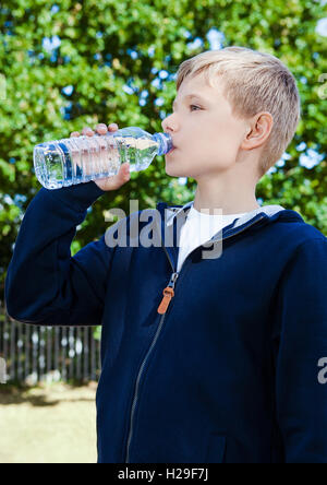 Young teenage boy drinking healthy still water in park summer time