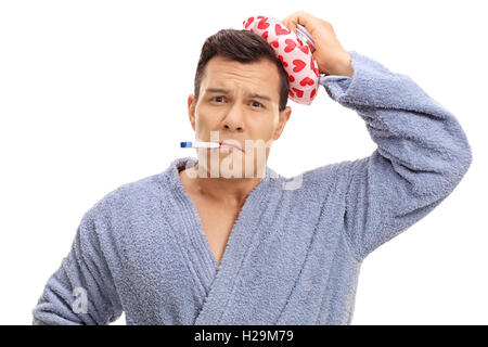 Sick guy holding an ice pack on his head and a thermometer in his mouth isolated on white background Stock Photo