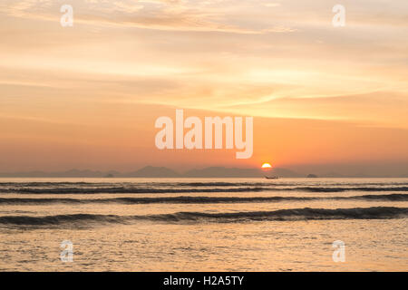 Sun setting behind mountain with fishing boat in foreground at Railey Beach, Thailand Stock Photo