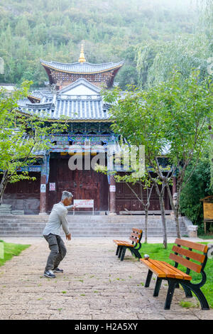 Oriental older man practicing tai chi in a park in front of a chinese temple in China Stock Photo