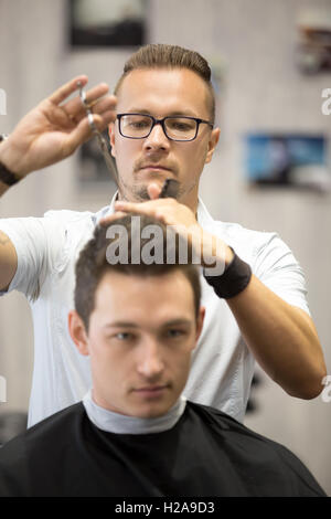 Working process in modern barbershop. Portrait of male hairdresser serving client, making haircut using metal scissors. Attracti Stock Photo