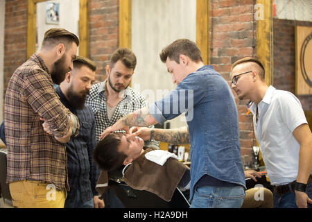 Teacher training group of students in beard shaving with metal straight razor in hairsalon. Interior shot of learning process in Stock Photo