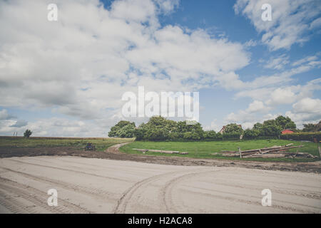 Large rural yard with tracks in sand and green fields Stock Photo