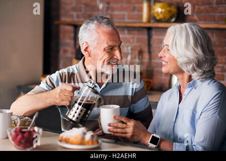 Grandparents drinking and pouring coffee at kitchen Stock Photo